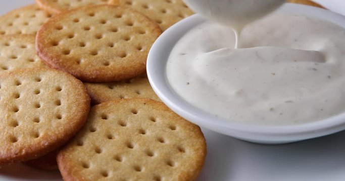 Close video of dipping a snack cracker into a bowl of ranch dressing with crackers to the side.