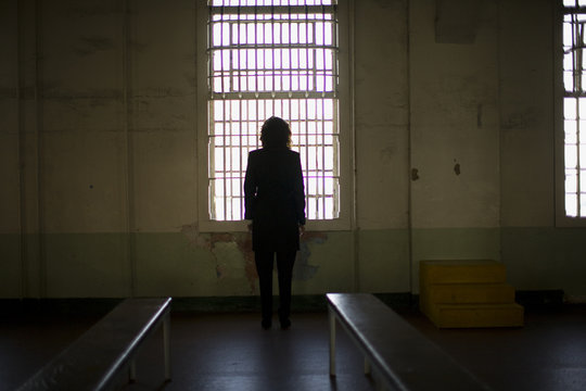 Mid-adult business woman standing in front of a barred window in a derelict building.