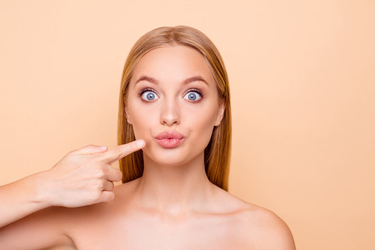 Pretty, charming funny attractive big-eyed girl pointing on pout lips with forefinger, showing effect after lifting procedure, dreaming about big lips isolated on beige background, perfection concept