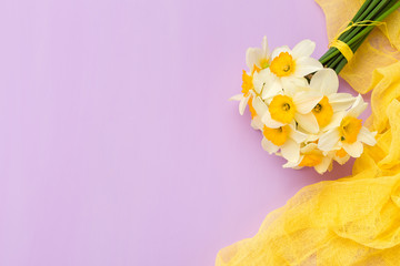 Daffodil bouquet with yellow textile decoration on violet pastel background with copy space.