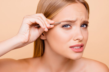 Patient, pretty, nude, natural model looking at camera plucking eyebrows with tweezers, having...