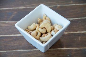 cashew nuts inside white bowl on a wooden table seen close up