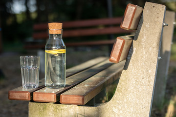 A bottle of water with lemon and a glass. A bench on which a refreshing drink is placed.