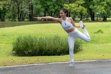 Beautiful young woman wearing white sports warm up before exercise. Sporty female warming up before running in the public park on tree background.