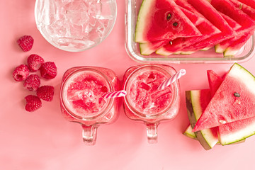 summer drinks concept. watermelon slices, ice cubes and smoothies in mason jar on pink fashion background top view. creative layout of watermelon and smoothies on pink top view