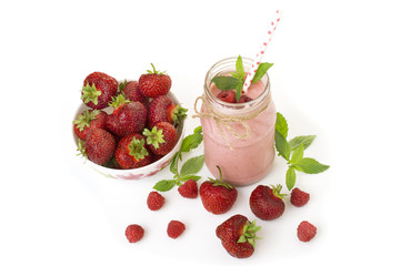 Pink strawberry and raspberry smoothie in a mason jar glass with straw and scattered berries