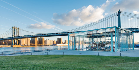 Manhattan Bridge at the Brooklyn Bridge Park. Lower Manhattan is bathed in early morning sunshine, blue sky with clouds a series of contrails and green grass.