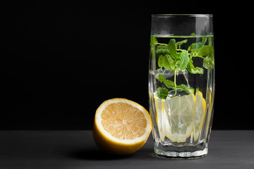 The concept of holidays and parties, food and drinks. Cold alcoholic cocktail mojito, lemonade with lemon, mint and ice in a glass on a black background. Vertical frame