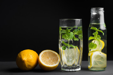 The concept of holidays and parties, food and drinks. Cold alcoholic cocktail mojito, lemonade with lemon, mint and ice in a glass and a bottle on a black background. Copy background space