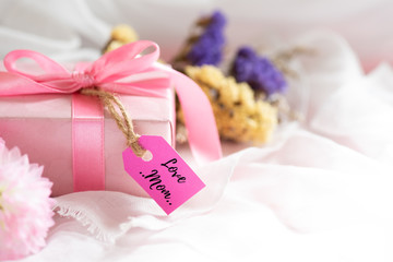 Happy mother's day concept. Gift box with purple flower, paper tag with LOVE MOM text and two handmade red heart on white cheesecloth background.