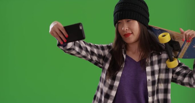 Relaxed Chinese skater girl using smart phone to take selfie on greenscreen