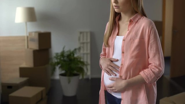 Sorrowful pregnant woman looking at boxes with things, husband leaving family