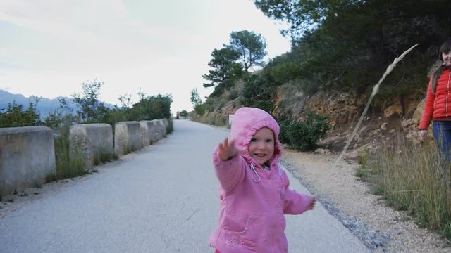 Naughty caucasian baby in the hood with herb strow laughing runs on mountain road trying to chase the camera. Happy childhood concept