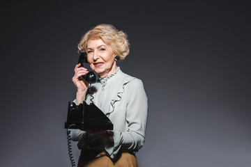 smiling senior woman talking by vintage phone on dark grey