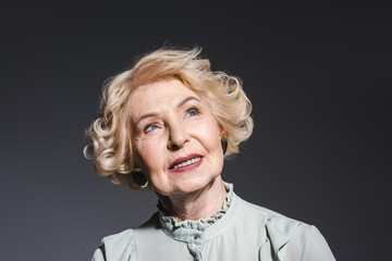 close-up portrait of thoughtful senior woman looking up on dark grey