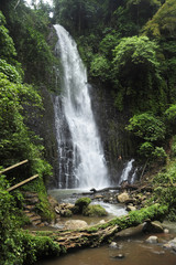 Fototapeta na wymiar A man sits beside Catarata Zamora, one of two impressive waterfalls in Los Chorros park in Costa Rica.