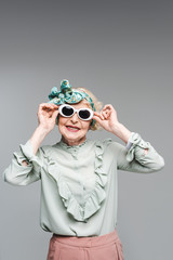 smiling senior woman in stylish headband and sunglasses isolated on grey