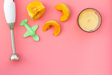 Make baby food at home. Puree with pumpkin near immersion blender, toy on pink background top view copy space