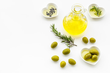 Fresh olive oil in glass jar near green olives and branch of rosemary on white background top view copy space