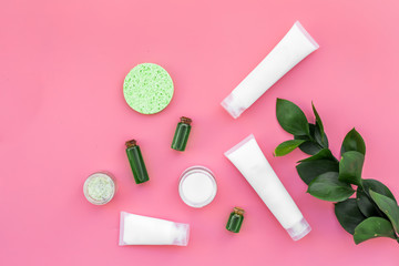 Cosmetics for skin care with natural ingredients. Eco cosmetics. Cream, lotion, oil, tonic near young green leaves on pink background top view copy space