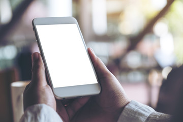 Mockup image of hands holding white mobile phone with blank desktop screen in cafe