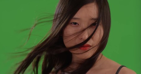 Young Chinese woman with hair blowing while smiling at camera on greenscreen
