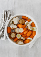 Healthy vegetarian food. Raw carrots, mushrooms and leeks in saucepan for steamed on white wooden table, top view. Steam cooking healthy food concept