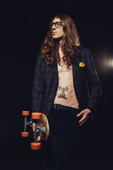 Fototapeta na wymiar handsome skater with long hair posing with longboard, isolated on black with backlit