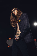 young stylish skateboarder posing with longboard, isolated on black with backlit