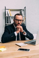 portrait of businessman in eyeglasses sitting at workplace with laptop in office