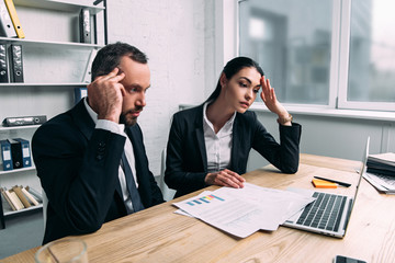 tired business colleagues in suits at workplace with papers and laptop in office