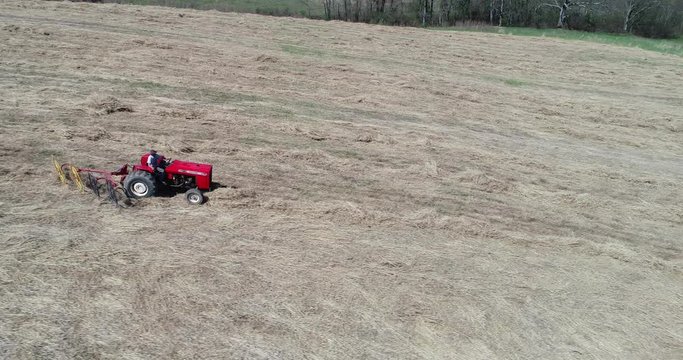 Side aerial view of tractor raking swithgrass in a field.