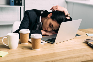 overworked businesswoman sleeping at workplace with laptop and coffee to go in office