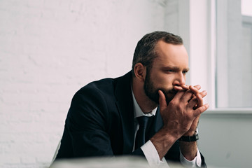 side view of tired and pensive businessman in suit looking away in office