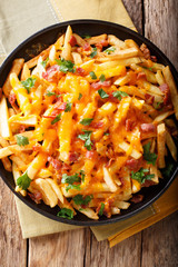 French fries with cheddar cheese, bacon and herbs close-up. Vertical top view