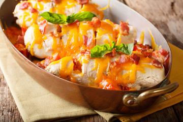 Spicy chicken fillet baked with bacon, tomatoes and cheddar cheese close-up in a frying pan. horizontal