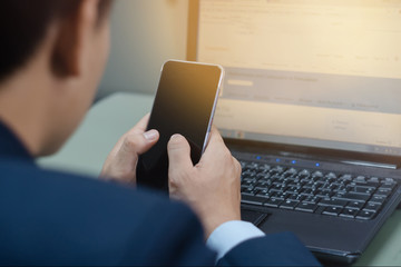 Close up of a young business man using cell phone and laptop to communicate and planing business project in the office. Business and finance communication with technology.