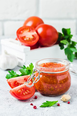 Homemade roasted tomato sauce in glass jar, garlic, pepper, salt on concrete background. Selective focus, space for text.