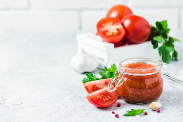 Homemade roasted tomato sauce in glass jar, garlic, pepper, salt on concrete background. Selective focus, space for text.