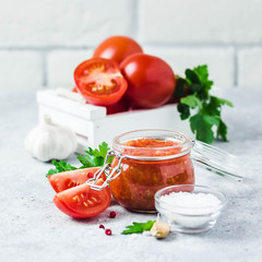 Homemade roasted tomato sauce in glass jar, garlic, pepper, salt on concrete background. Selective focus, space for text.