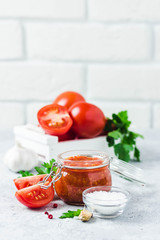 Homemade roasted tomato sauce in glass jar, garlic, pepper, salt on concrete background. Selective focus, space for text.