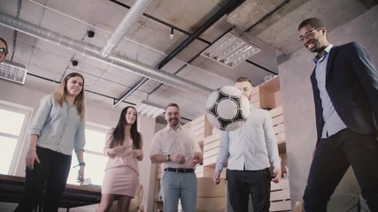 Multiethnic office colleagues play with football during break. Happy employees hold casual physical activity slow motion - Powered by Adobe