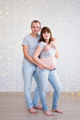 family and parenthood concept - full length portrait of pregnant couple over brick wall