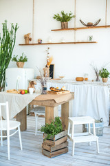 Kitchen in rustic style in summer. Spring light textured kitchen with an old fridge, wooden table. A wooden tray with a vase, willows, a white cup, a green and red apple, a paper bag with food