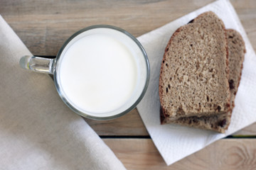 A glass of milk next to a slice of rye bread on the table