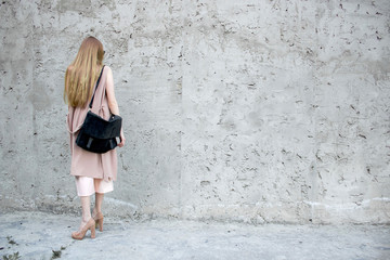 Red hair girl in pink look, with black leather bag, pose on the concrette background. Fashion and stylish concept.