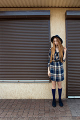 Red hair girl in plaid shirt and vintage hat, with brown backpack pose on the street. Fashion and stylish concept.
