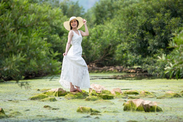 Fototapeta na wymiar Asian beautiful women wearing white dress in the forest on the creek with sea weed and standing on the stone.