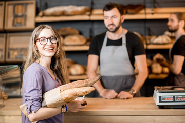 Woman buying bread in the bakery shop with man sellers