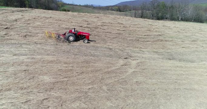 Aerial view at side of tractor with star wheel rake raking switchgrass in a field.